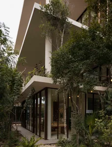 Modern building exterior made of concrete with large glass windows and plants surrounding it.