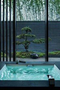 Modern hot tub with glass railing overlooking lush greenery and bamboo forest.