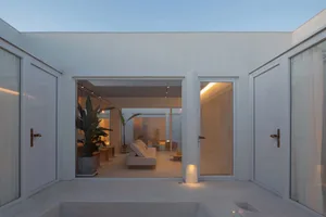 A minimalist living room with concrete walls and floor, featuring a white sofa and illuminated by warm lighting from the ceil