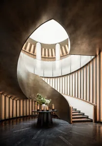 Modern, metal spiral staircase with a brass finish, leading to a glass-paneled ceiling.