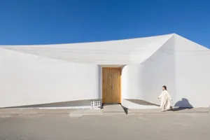 A minimalist white building with a concrete facade and a wooden door.