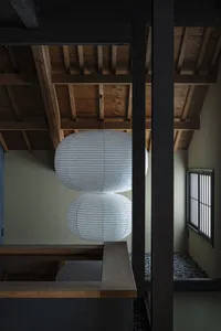 白色紙燈籠懸掛在木樑上，置於混凝土房間內，自然光從窗戶灑入。