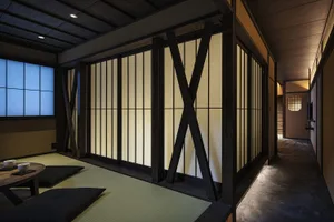 A photograph of a traditional Japanese residential room with wooden walls, sliding doors, and tatami mats.