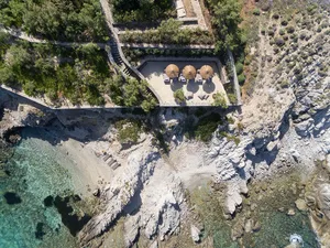 Aerial view of a luxurious vacation getaway featuring stone cliffs, pool terraces, and sunbeds.