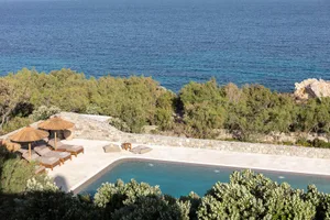 A stone vacation home with a rockpool and Mediterranean vegetation.