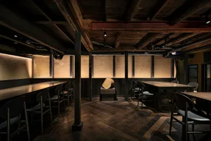 Industrial-themed restaurant with wooden tables and chairs, exposed wooden beams, and warm lighting.