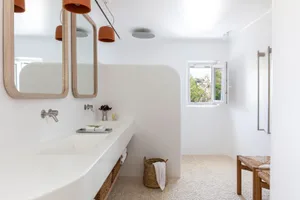A minimalist bathroom featuring white concrete walls, a double sink vanity, and a terra cotta pendant light fixture.