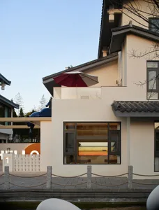 Modern residential exterior with white walls, dark roof, and glass windows with a hanging outdoor sofa.