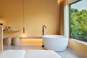 Minimalist bathroom featuring a white freestanding tub, ceramic floor tiles, and a large window with a view of greenery.