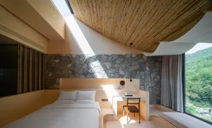 A serene, minimalist bedroom with concrete walls, a skylight, and a view of the mountains.