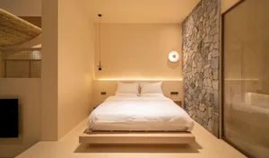 Minimalist bedroom featuring a concrete platform bed with stone accent wall and ambient lighting.