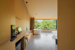 現代極簡酒店套房，混凝土牆面與地板，設有可俯瞰綠意的浴缸。