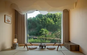 A minimalist living room with natural materials, featuring two cushions, a small wooden table, and a large window overlooking