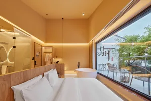 Minimalist bedroom with white furniture and a large window overlooking a garden.