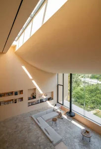 A modern minimalist living room with concrete walls, glass windows, and a comfortable seating area.
