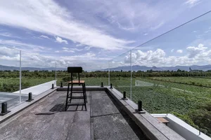 A modern outdoor patio with a concrete floor, glass railings, and a high-back chair overlooking green fields and mountains un
