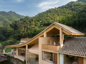 A modern residential building with a wooden exterior and glass windows overlooking a lush, forested hillside.