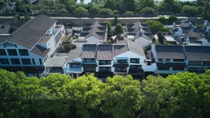 Aerial view of a traditional white village with gray-tiled roofs and green leafy trees.