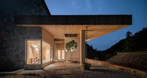 A modern residential building with stone, concrete, and wooden materials outdoors at dusk.