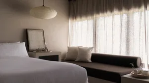 A modern bedroom featuring soft textiles on the bed and window seat, with a minimalistic design and warm lighting.