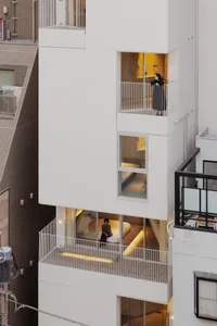 Modern urban apartment building with white cladding, balconies, and interior lighting.