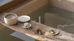A rustic wooden bathtub caddy holds ceramic containers filled with bath salts, accompanied by a smoking incense holder.