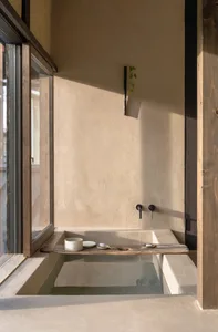 Concrete bathtub in a minimalist bathroom with a wooden shelf holding a ceramic cup and a small plate.