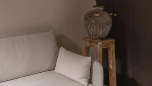 A minimalist interior space featuring a wooden stool and beige fabric sofa.