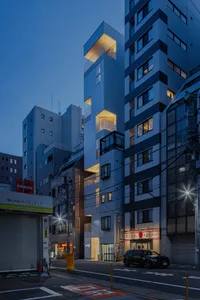 A modern building with metallic aluminum cladding, featuring a unique angular design and illuminated balconies.