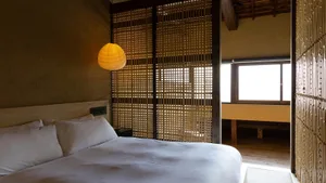 A minimalist bedroom with a bed, white sheets, and a wooden headboard.