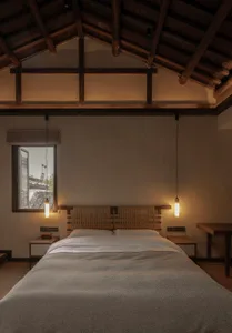 A modern minimalist bedroom with a wooden bed frame, grey bedding, and industrial-style pendant lights hanging from the ceili