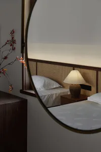 A minimalist bedroom featuring a white bed with a cane-weave headboard and a warm, ambient light.