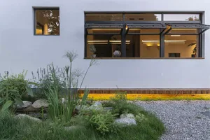 Modern house exterior made of concrete with large windows and a garden.