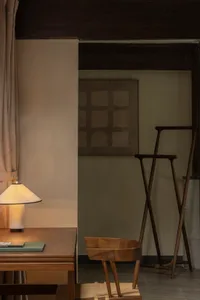 A modern minimalist living room featuring a wooden chair, a simple table lamp, and a minimalist artwork.