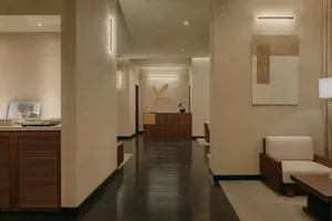 Modern, minimalist hotel reception area with sleek, dark wood flooring, beige seating, and a sleek reception desk with the ho
