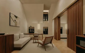 A minimalist living room with a white sofa, wooden armchair, and wooden desk.