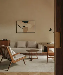 A minimalist living room with neutral-toned furniture and decor, featuring a sofa, armchair, coffee table, and abstract artwo