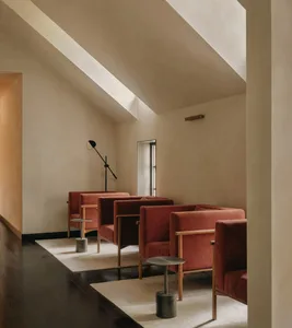 A minimalist living room with red fabric sofas, wooden tables, and concrete floor.