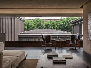 A minimalist living room featuring wooden furniture, leather accents, glass windows, and concrete flooring.