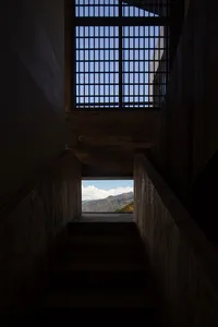 A minimalistic staircase made of wood, viewed from below, with a view of mountains through a window.
