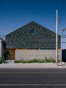 A modern house exterior with green shingles, concrete walls, and a circular window.
