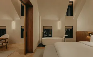 Modern minimalist bedroom featuring a white bed, white bathtub, and beige walls with plaster finish.