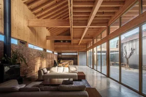 Modern minimalist living room with exposed wooden beams, large glass windows, and a comfortable sofa.