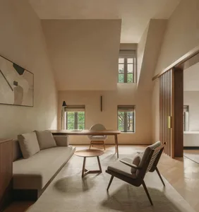 A minimalist living room workspace featuring a large couch, wooden table, and chairs, with light-colored fabrics and wooden e