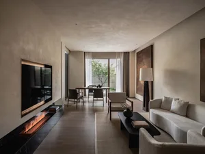 A modern living room with neutral tones, featuring a fireplace, a couch, and a dining area with chairs.