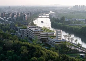 A modern office building with a concrete exterior and a landscaped riverfront.