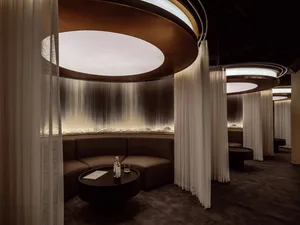 Modern restaurant interior with white curtains, circular lighting, and a circular table with a bottle and glass.