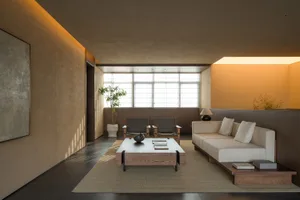 A modern, minimalist living room with beige walls, a white sofa, and a wooden table.
