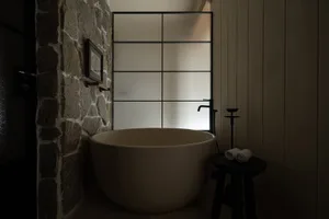 A minimalist bathroom with a stone wall, glass partition, and metal bathtub fixtures.