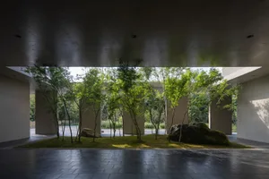 Minimalist concrete interior with greenery and large rocks, featuring modern architecture and a spacious open-plan layout.